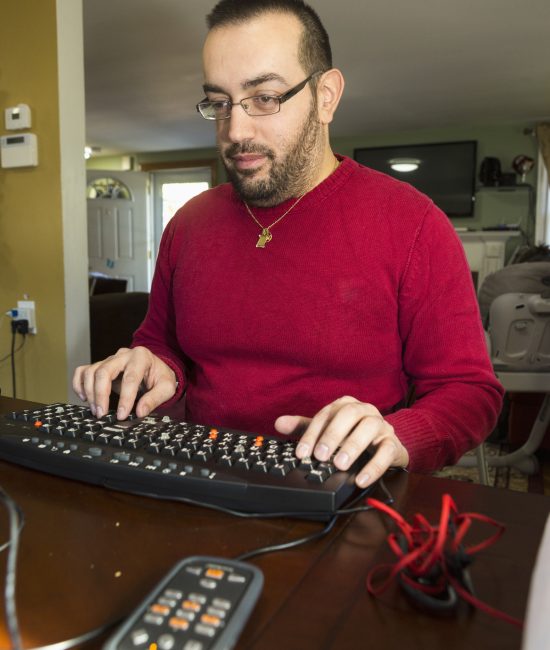 man with low vision tying on an alternate keyboard with an audio recorder next to him.